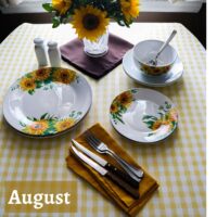 August table sunflowers and sunshine with sunflowers in a vase and design on the dishes on a yellow and white checkered tablecloth