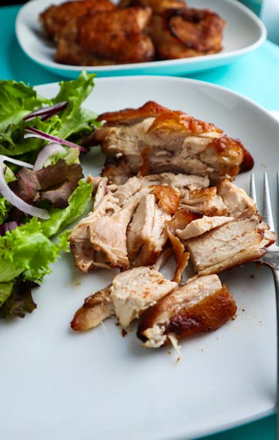 marinated chicken thighs on a white dinner plate with salad served and a platter of chicken in background