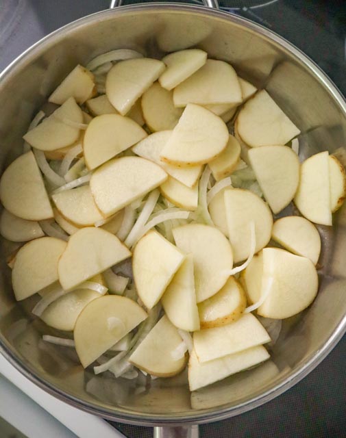 sliced potatoes and onions in a skillet with olive oil