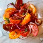 tomato salad in a glass bowl made with heirloom tomaotes red onion and basil.