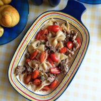 grape tomatoes and italian sausage meat over pasta served in oval dish with checkered yellow tablecloth