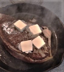 london broil steak being seared in a skillet with butter melting on top 