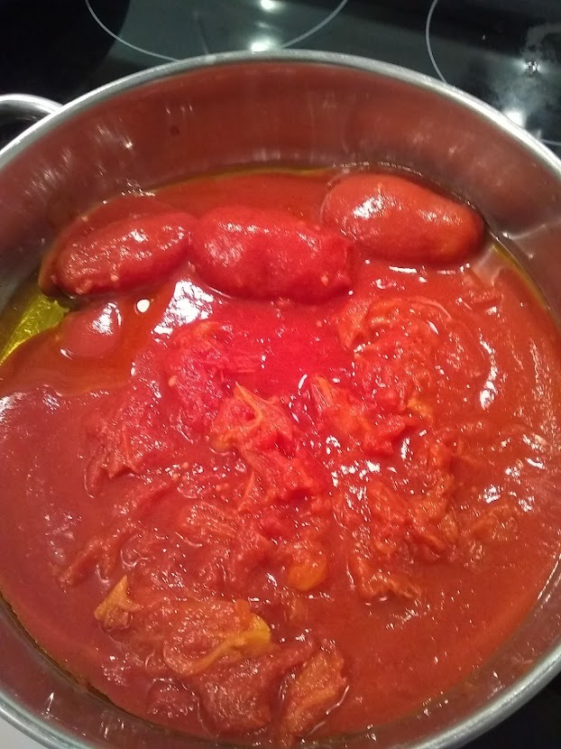 whole peeled tomatoes in a skillet with some hand crushed and some whole