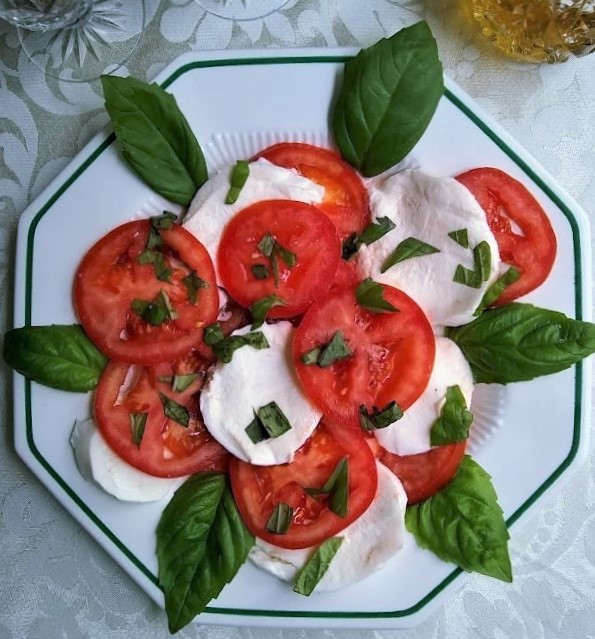 caprese salad tomato mozzarella cheese and basil served family style on an octagon ivory plate 