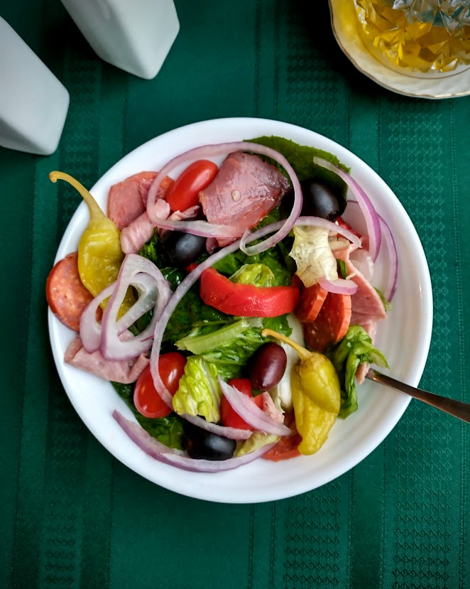 Antipasto salad served in a white bowl with a green tablecloth
