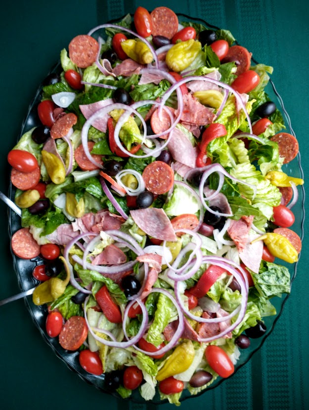 platter of antipasto salad made with fresh lettuces grape tomatoes olives and other brined vegetables and deli meats