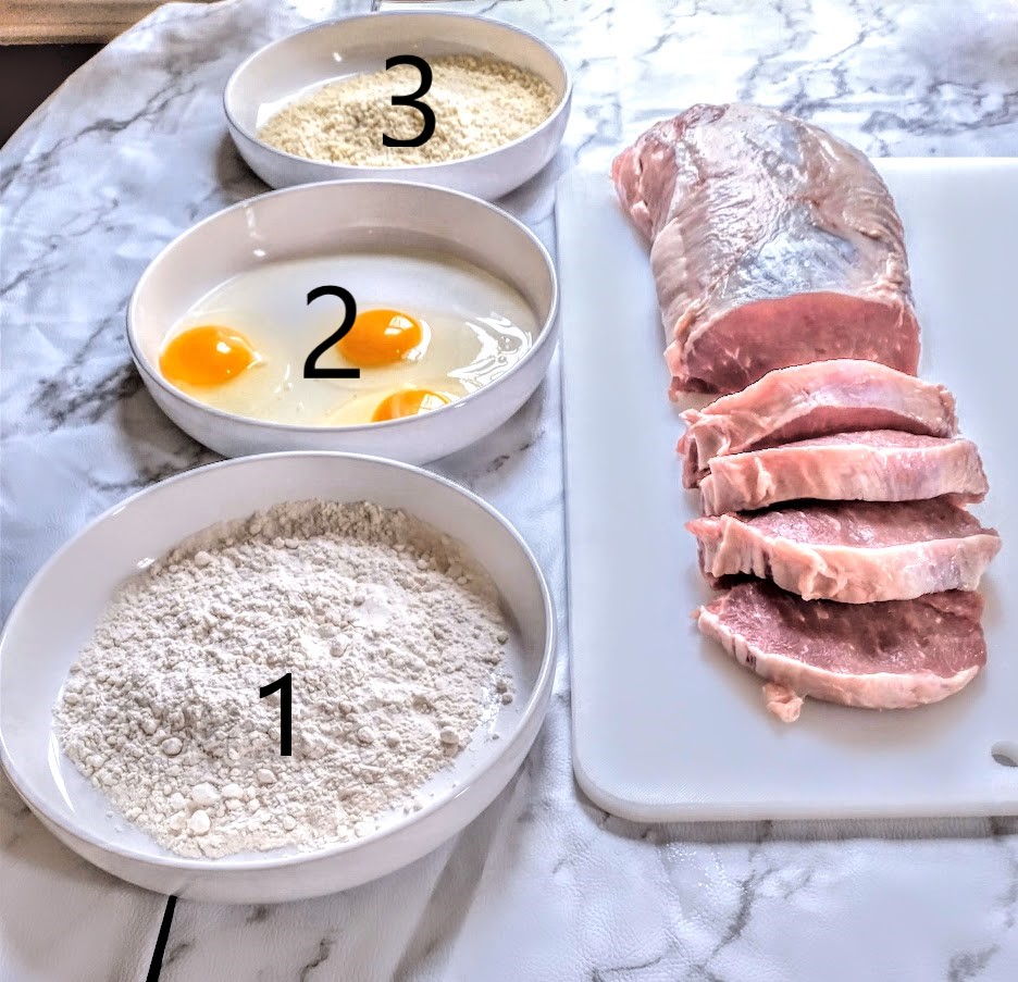 a pork loin being chopped into one inch cutlets three bowls to do the breading containing flour eggs panko crumbs