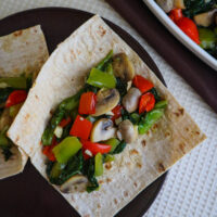 an all vegetable saute for wraps with escarole green and red peppers mushrooms and garlic on a wrap served on brown plate