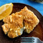 baked cod with garlic butter sauce served with lemon on brown plate