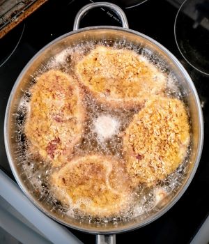 skillet with four breaded cutlets deep frying