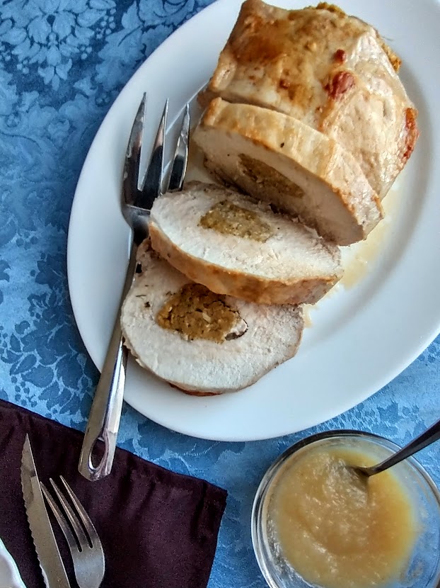 stuffed pork loin roast on a serving platter with a side dish of applesauce