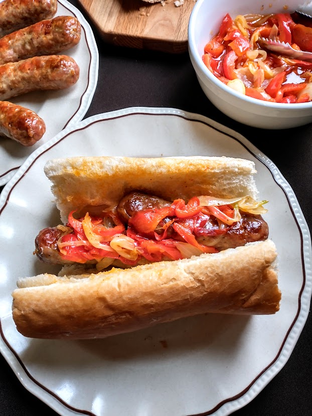 two italian sausages covered in sautéed pepper and onion served on french bread