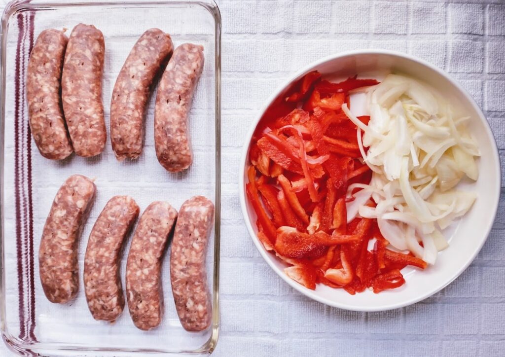 italian sausage links in a baking dish cut red pepper and sliced onion