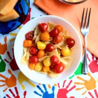 multi colored grape tomatoes with bowtie pasta served in a white bowl with shredded cheese and melon on the table