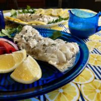 cod with creamy lemon pepper sauce on cobalt dish with lemon and tomatoes with sauce in background