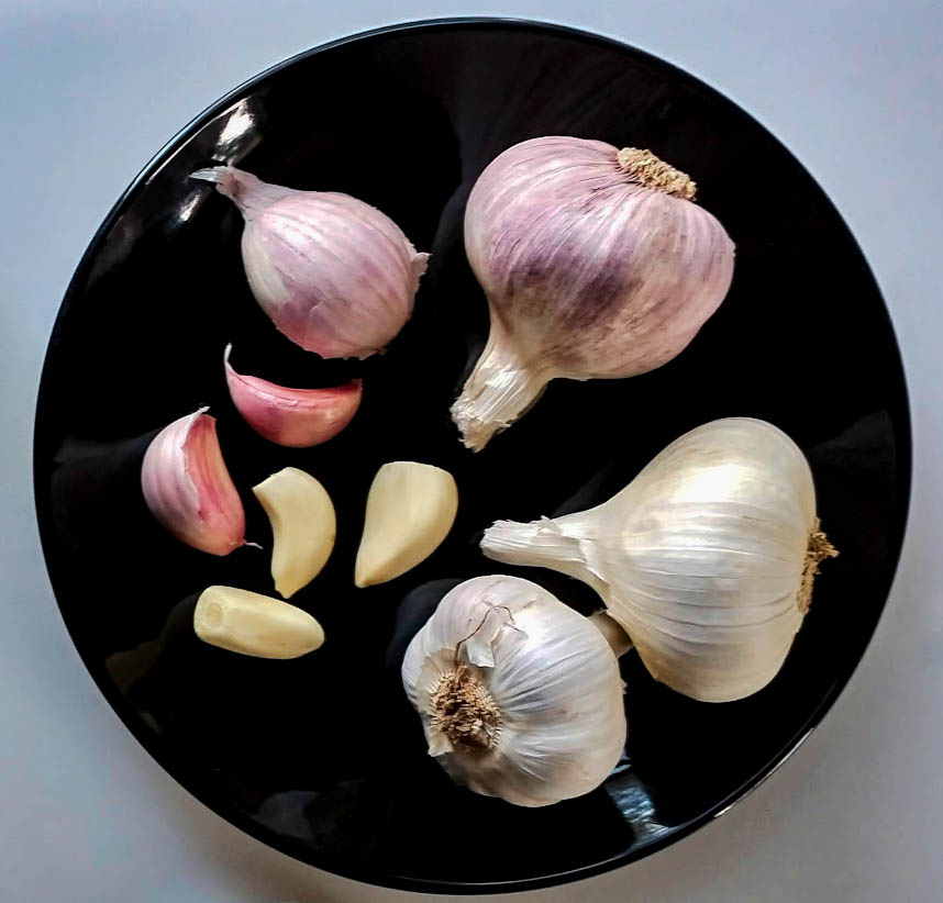 a black plate with fresh garlic heads and fresh garlic cloves