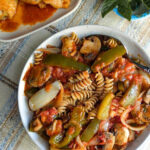 chicken cacciatore ,a serving bowl with cacciatore vegetables in sauce mixed with rotini pasta chicken in background
