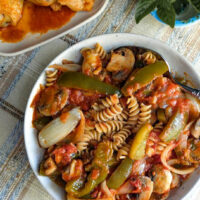 chicken cacciatore ,a serving bowl with cacciatore vegetables in sauce mixed with rotini pasta chicken in background