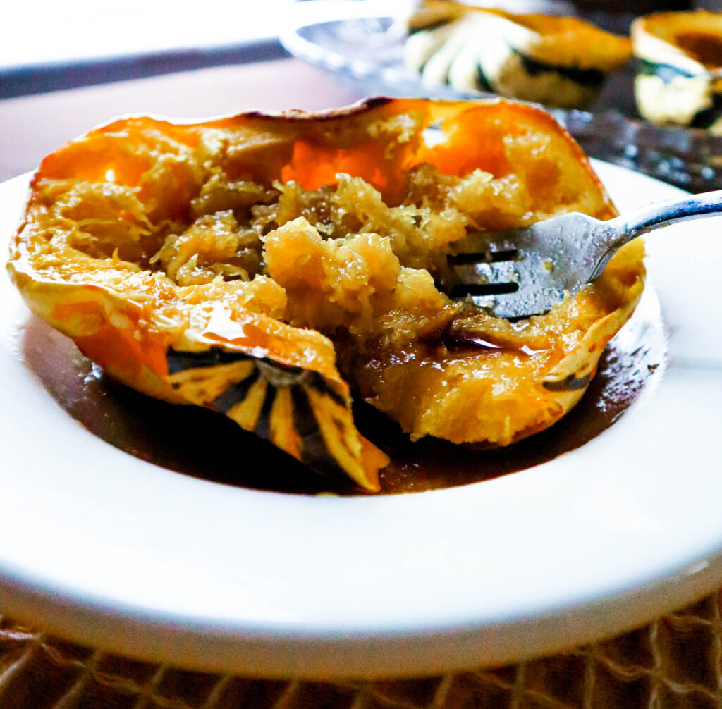 one half of a colorful fall squash baked with butter brown sugar and maple syrup served in a shallow bowl