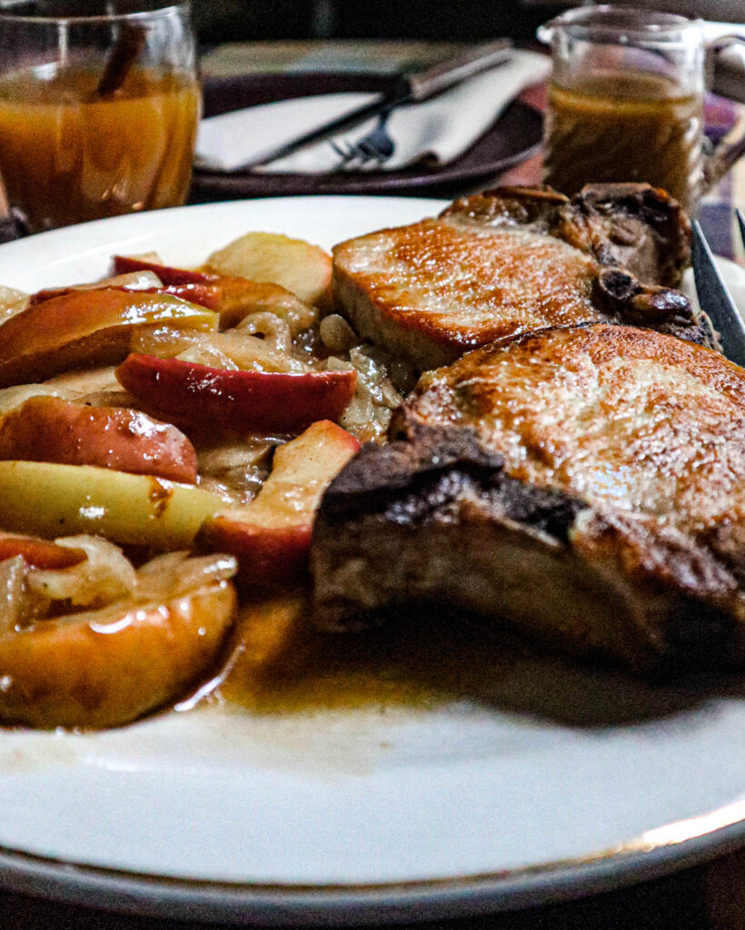 seared pork chops on a platter with an onion and apple side dish in a cider sauce