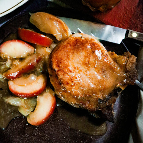 pork chops apples and onions in a homemade cider sauce served on a brown plate