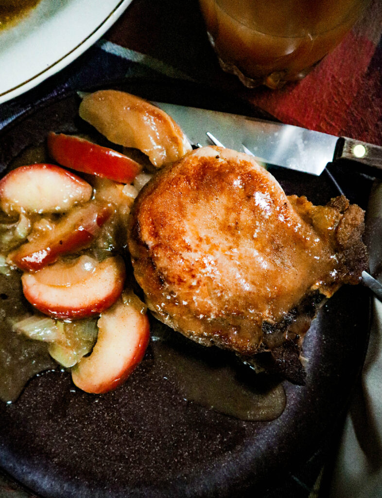 pork chops apples and onions in a homemade cider sauce served on a brown plate