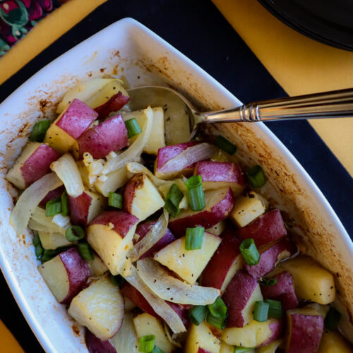 rectangle serving dish with chopped red potato and onion in a butter sauce topped with scallion greens