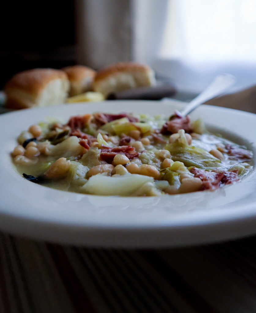 bowl of cabbage and beans served in white wide lipped bowl with rolls on the table