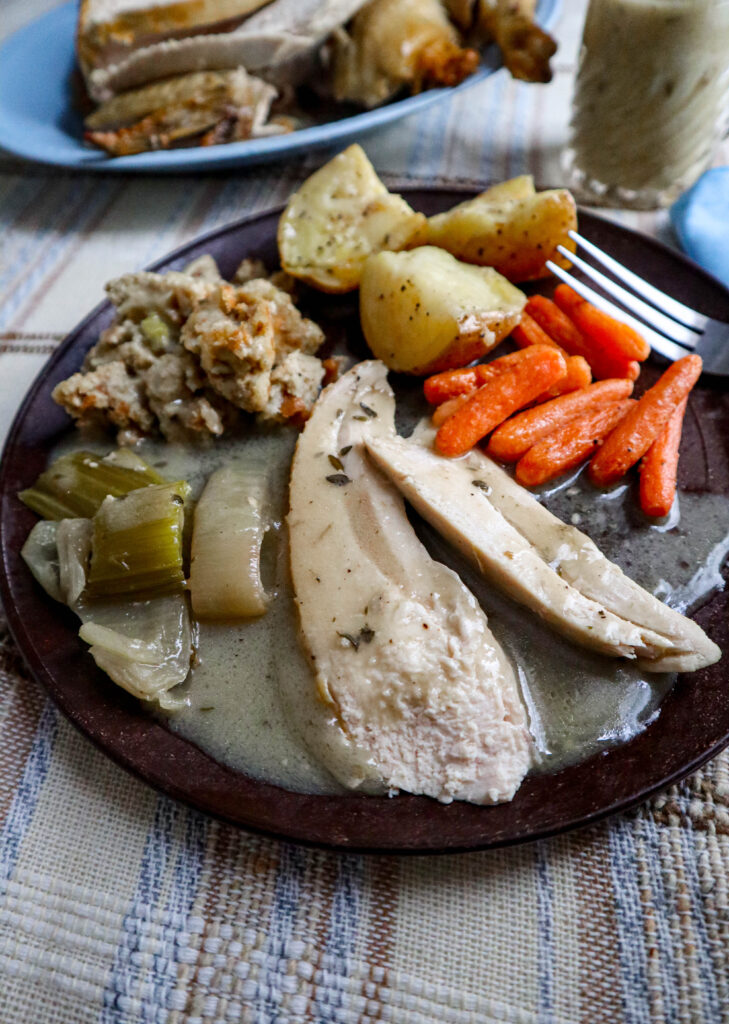 chicken dinner served on brown plate with stuffing carrots potatoes carrots roasted celery and onion and sliced chicken with gravy