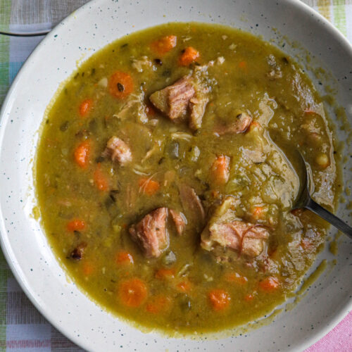 split pea soup with ham carrots celery onion and herbs served in a large white bowl