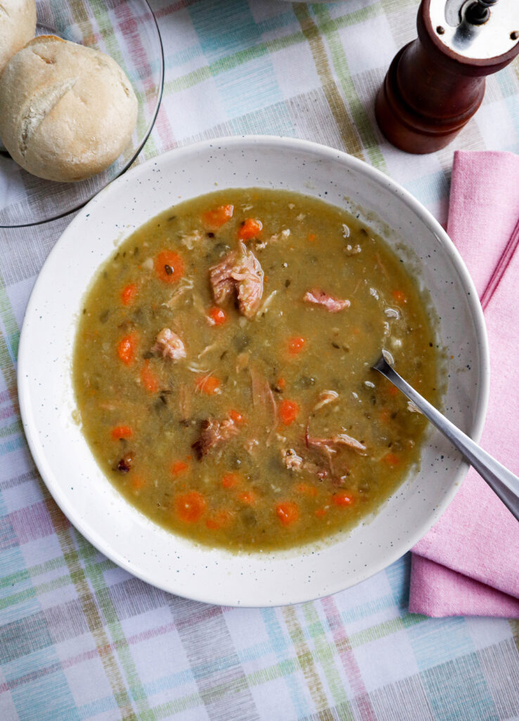 split pea soup with ham carrots celery onion and herbs served in a large white bowl