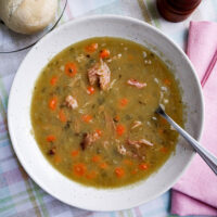split pea soup with ham carrots celery onion and herbs served in a large white bowl