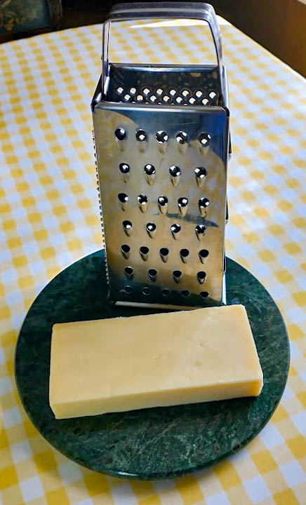 a block of cheddar cheese and a box grater