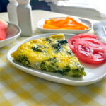 slice of broccoli frittata served with sliced tomato on a white square plate