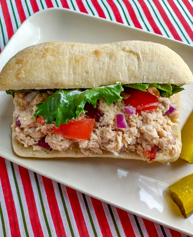 an italian tuna salad sandwich on a ciabatta roll on a plate with pickles. 