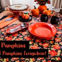table setting of orange and black with pumpkin pie pumpkins and a tablecloth of pumpkins on a black background