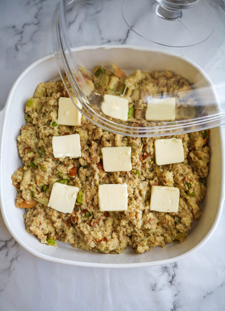 uncooked stuffing with pats of butter on top in a baking dish with a cover