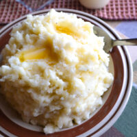 heaping bowl of mashed potatoes with butter dripping from top to bottom table and dishes in ivory and brown
