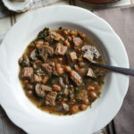 beef and beans stew with mushrooms and spinach served in a white bowl