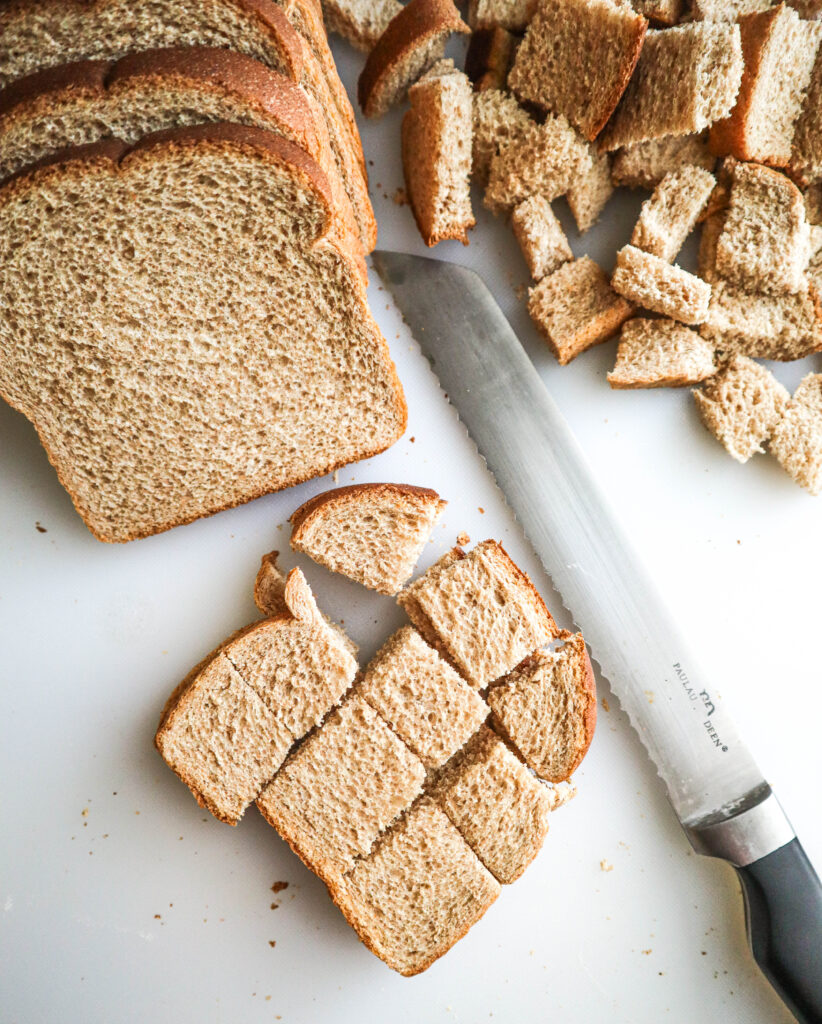 a loaf of whole wheat bread being cut into cubes