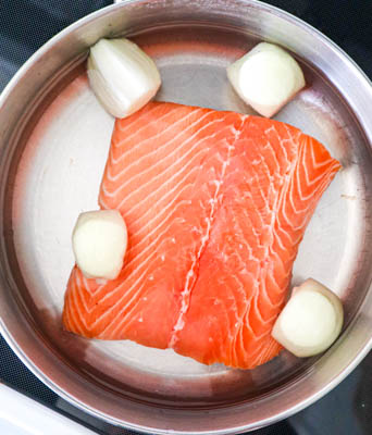 salmon in water with quartered onion in skillet