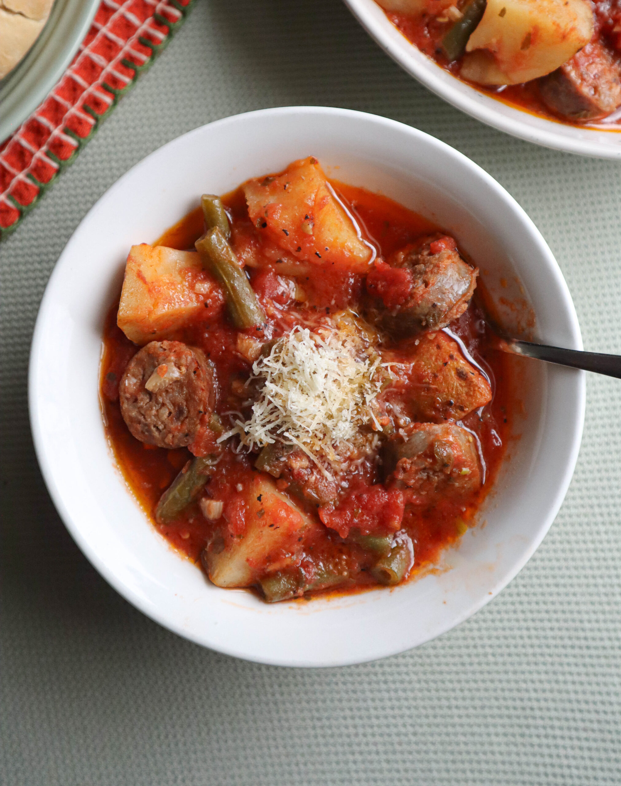 italian sausage stew with potato and green beans in tomato sauce served with grated cheese in a single serving bowl 