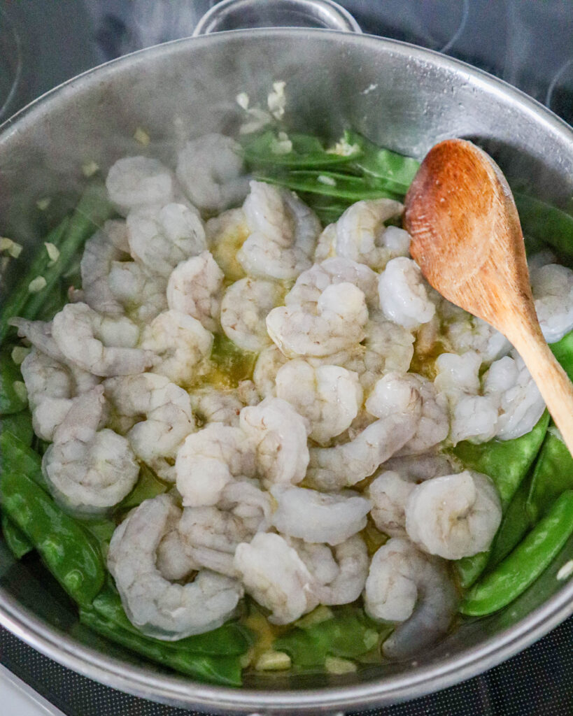 adding raw shrimp to the skillet with the pea pods and olive oil garlic sauce