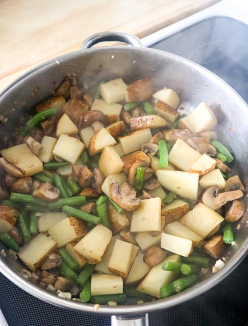 steaming skillet with potatoes green beans mushrooms and garlic