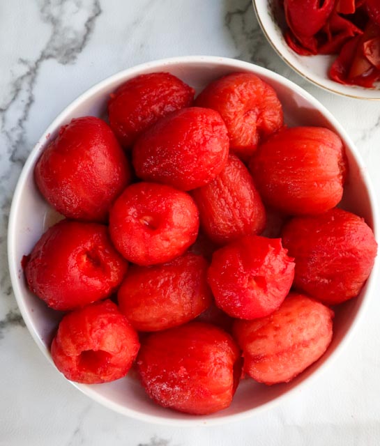 a white bowl plum tomatoes that have been peeled