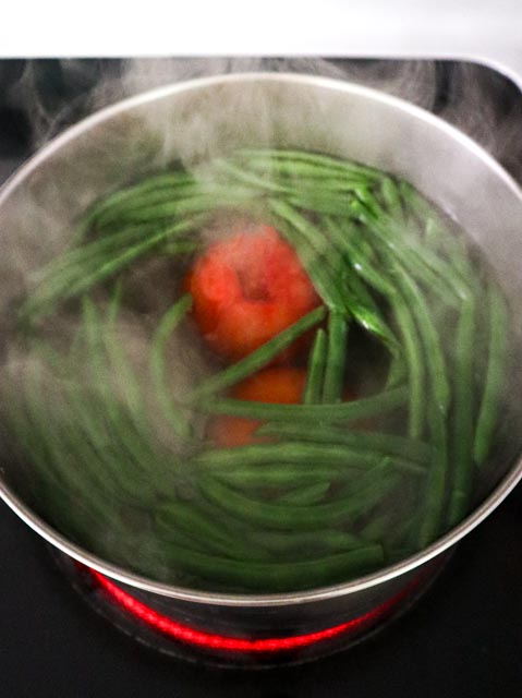 string beans and tomatoes are blanching in a pan